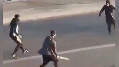 Three men wearing hats and/or masks confront each other in the street. They all appear to be holding knives/bladed weapons.