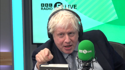 Boris Johnson wearing a suit and headphones speaking into a mic in a BBC radio studio