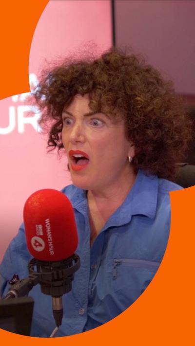 Annie Mac looks shocked in the Woman's Hour studio. She has curly brown hair and wears a blue  shirt 