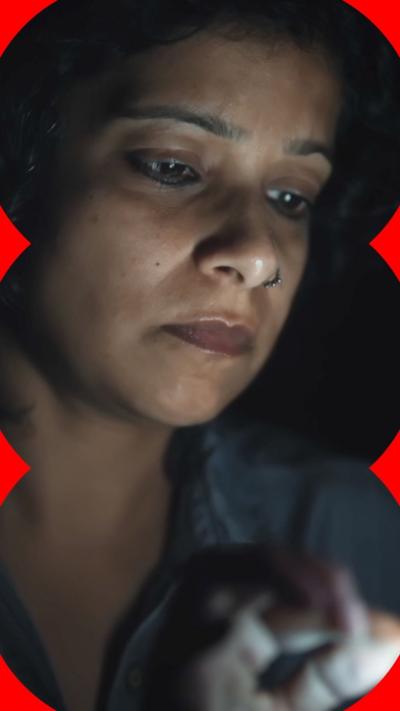 A woman in a dark room with the light from a phone shining on her face.