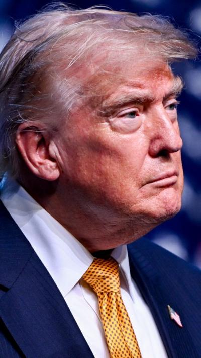 Donald Trump looks off camera towards the left as he wears a blue suit and yellow tie.