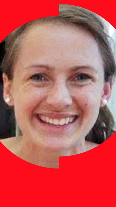 Head-and-shoulders portrait of a person with hair tied back, wearing pearl stud earrings and a light-coloured top, facing the camera indoors.