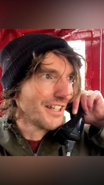 Man with straggly hair in a red phone box