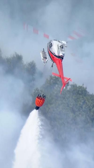 A helicopter drops water from a bucket on smokey forest