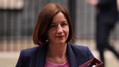 Bridget Phillipson leaves 10 Downing Street. She is wearing a navy blazer and a pink blouse and is holding a red binder.