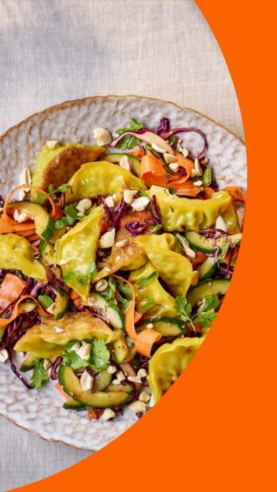 Dumpling salad on a round plate with a small dish of sauce on the side