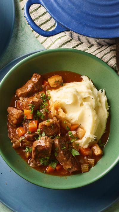 Top down view of a green bowl containing mashed potato and beef stew
