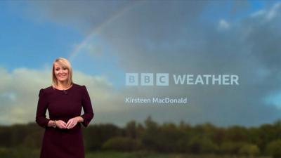 Woman wearing burgandy dress, with blue sky and rainbow in the background.