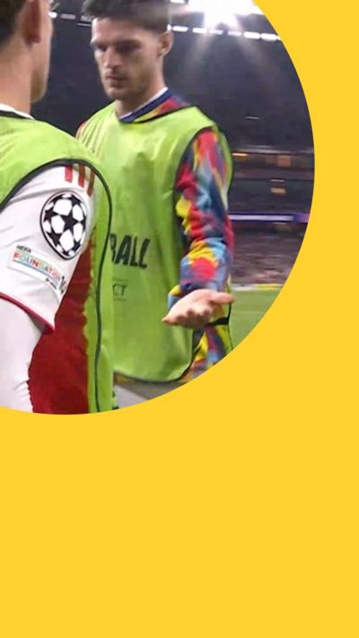Declan Rice holds out his left hand to teammate Max Dowman in the football pitch. Both wear green bibs