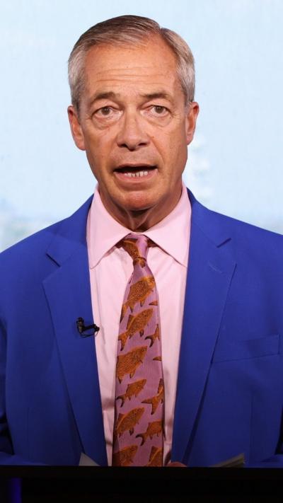 Nigel Farage in a blue suit with a pink shirt and pink tie with orange fish on