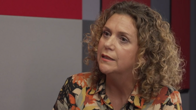 Hannah Ingram-Moore sitting down in an office room, with curly brown but highlighted blonde hair and wearing a floral top.