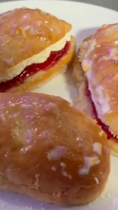 A close up of iced buns on a white plate. The buns have been glazed with white icindg and cut in half. In the centre is whipped white cream and red jam.