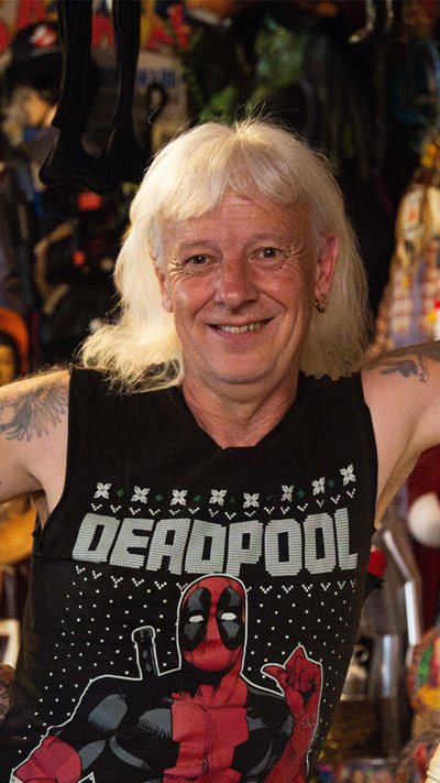 Man with long grey hair in a Deadpool vest leaning on a Nasa statue