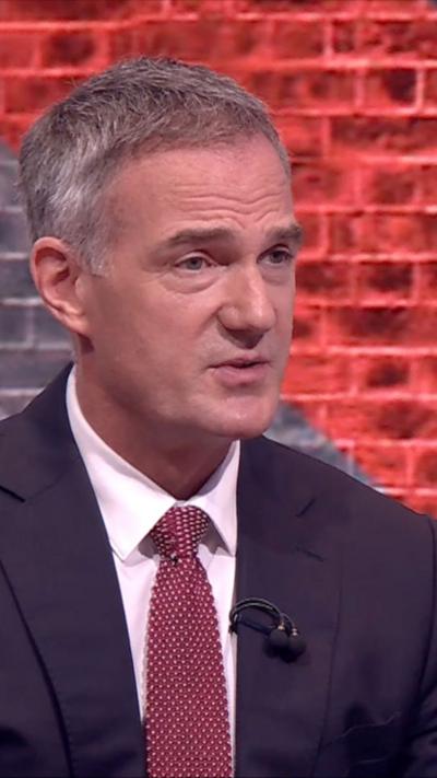 Kyle has grey hair and wears a suit in the TV studio