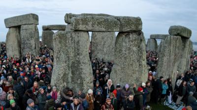 People stand at Stonehenge just after sunrise