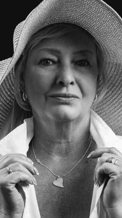 Woman wearing a large sunhat, white shirt and a heart necklace with a black and white filter over the picture.