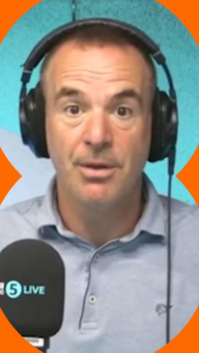 Martin Lewis has short day hair, is wearing headphones and a blue polo-shirt and had his hands up to the side of him.