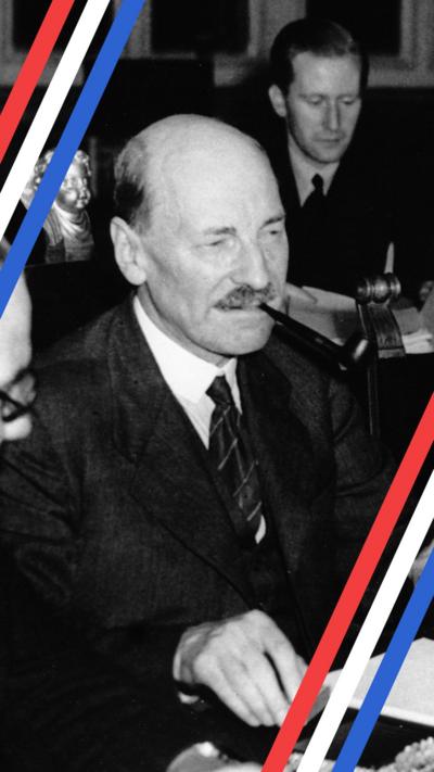 A Black and white photo of prime minister Clement Attlee looking serious while smoking a cigar and wearing a suit. He is holding a box of matches in his right hand above the table. He is sat in a meeting behind a table surrounded by other men at the Potsdam Conference in 1945.