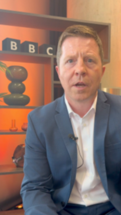 A man in a suit infront of a BBC logo