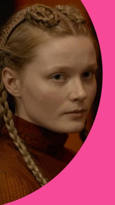 A young woman with a steely look on her face. She has blonde hair with plaits 