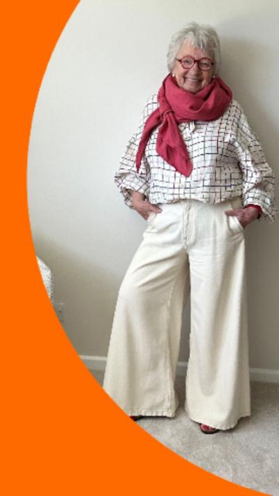 A woman with short grey hair poses in cream trousers and a patterened shirt
