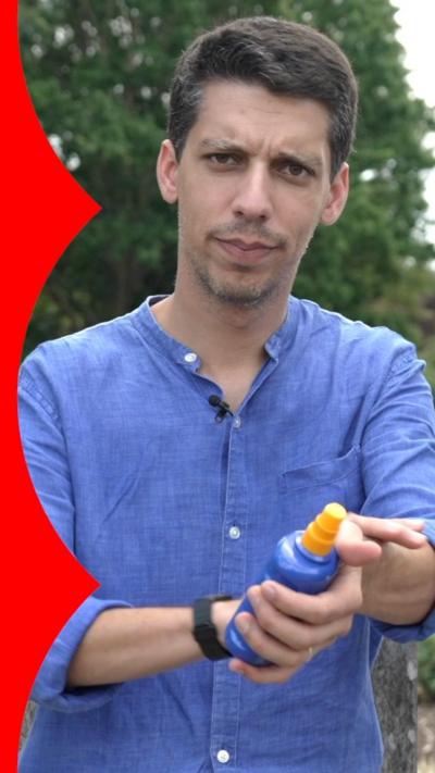 A man with short brown hair wearing a blue shirt holds a bottle of sun cream