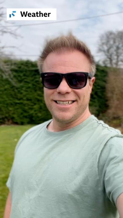 Weather forecaster Simon King stands in a garden wearing a T-shirt and sunglasses