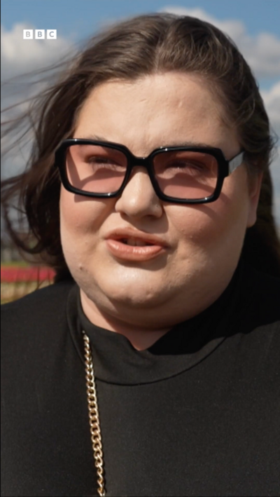 Woman in a black top with glasses and black hair stands in a tulip field.