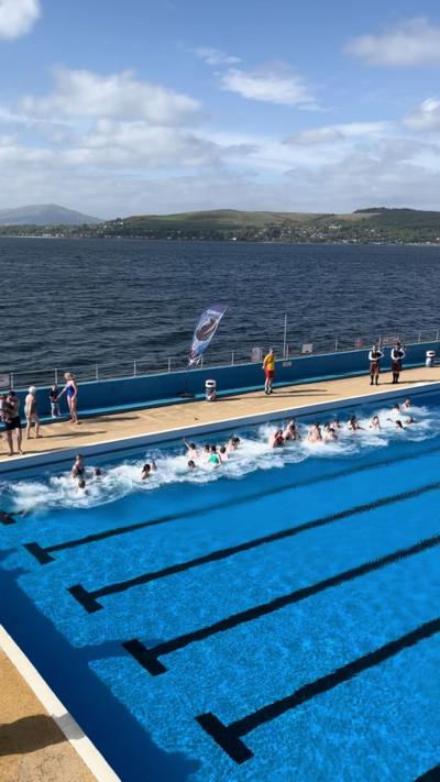 Water splashes as swimmers jump into an outdoor swimming pool by the sea