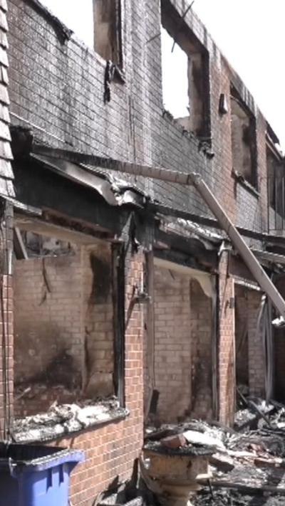The outside of a wrecked home with burnt out windows and rubble on the ground.
