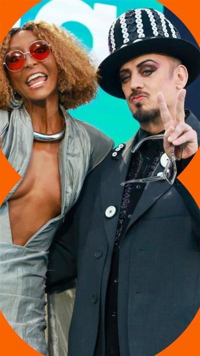 SENHIT and Boy George both make the peace sign. She wears a silver top, he wears a black suit and black and white hat