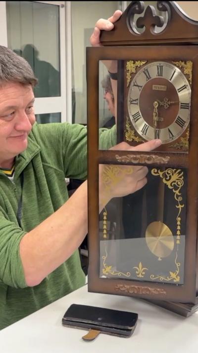 A man with grey hair is repairing a large wooden clock. 