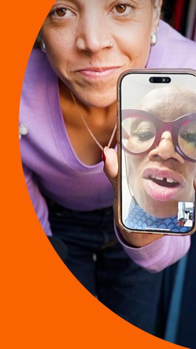 Miquita stands close to the camera, holding her phone up where you can see Andi Oliver on a video call