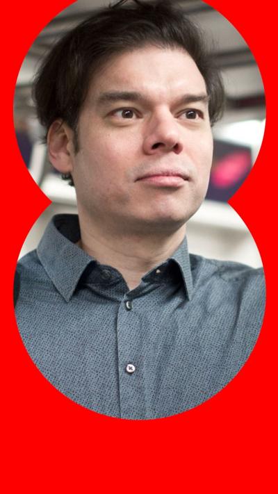 A man with short, black hair stands on a train