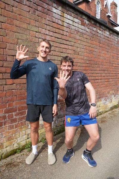 Two runners in blue running gear stood against a brick wall