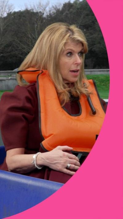 Kate Garraway is wearing a maroon top and bottoms, and an orange life jacket as she sits inside a blue pedalo
