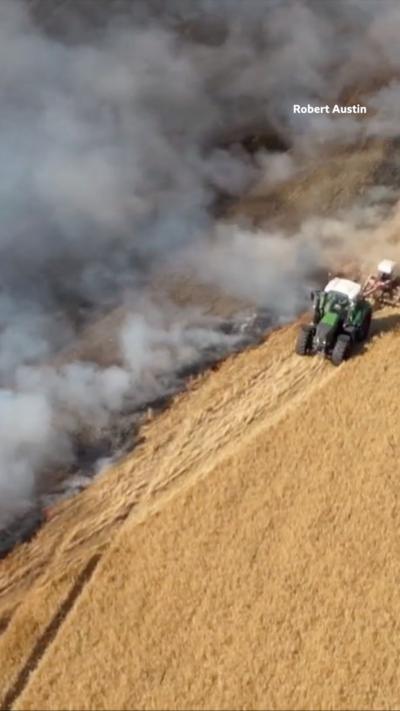 A drone shot of a tractor driving in a field separating a fire from untouched crops