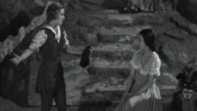 Dorothy Dickson, in costume as Dick Whittington, singing a love song to "Alice", played by Jean Adrienne, as part of a pantomime at the Garrick Theatre in 1932