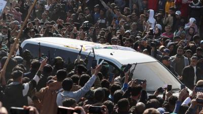 Crowds stand around vehicle, with many holding their phones up