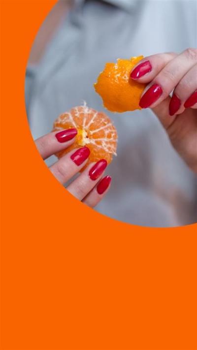 A woman peels a tangerine. She wears a light blue shirt and has bright pink nail varnish