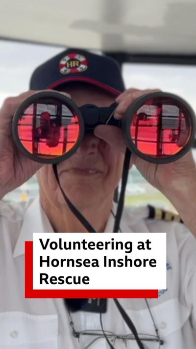 A man wearing a baseball cap is holding a pair of binoculars to his face 