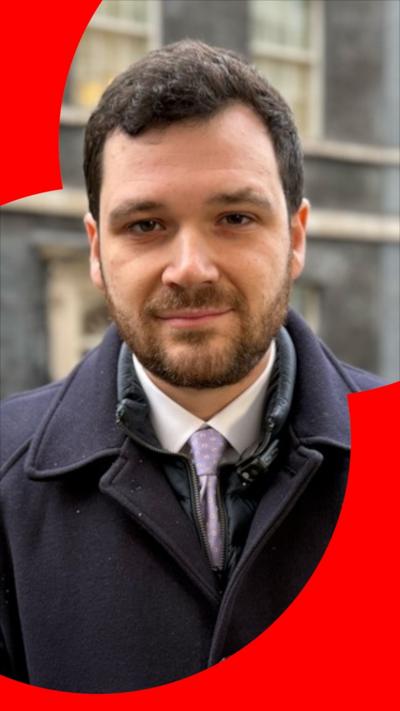 A man, Henry Zeffman, with short brown hair and a dark blue jacket, stands outside 10 Downing Street