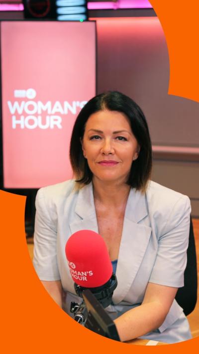 A woman with brown, bobbed hair sits behind a microphone
