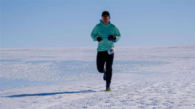 Mr Holborn, wearing an orange sun visor, teal hoodie and black trousers, running along the ice of Antarctica