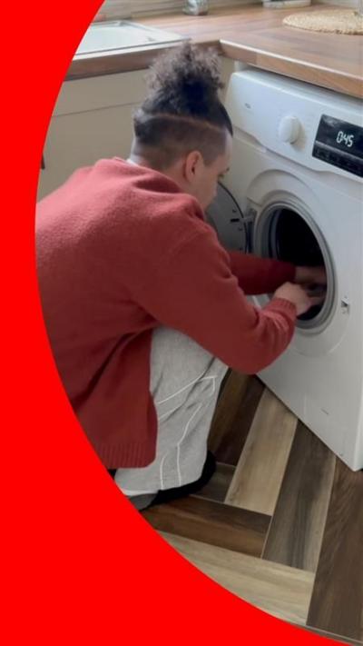 BBC Journalist Tyler Edwards wears a dark orange cardigan and crouches down to load laundry into a washing machine.