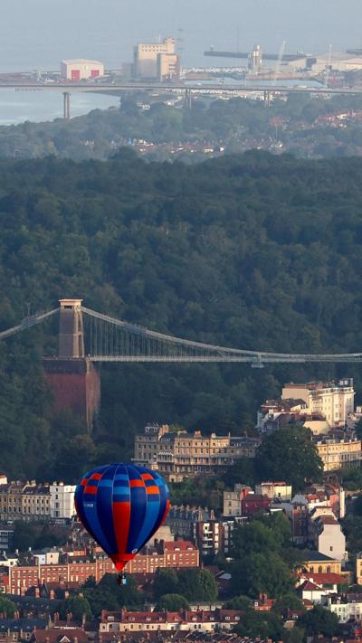 A hot air balloon flies in front of the Clifton Suspension Bridge on a sunny day