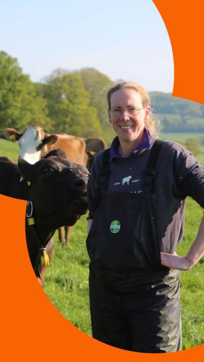 Dairy farmer Lorna Burdge stands in a field wearing overalls, with cows behind her