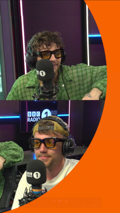 Tom Grennan wearing a green shirt and yellow-tinted glasses, sat in front of a Radio 1 microphone and Roman Kemp in yellow-tinted glasses, sat in front of a Radio 1 microphone