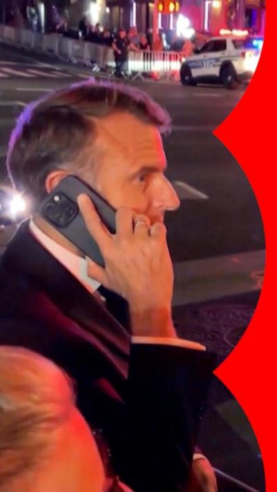 Side view of President Macron talking on the phone with a street at night behind.