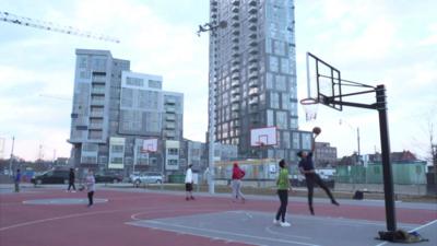 People play basketball with modern apartments in the background